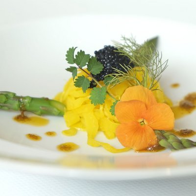 Ihr Wellnesshotel im Allgäu Feine Gourmetplatte mit grünem Spargel, essbarer Blume und Kaviar auf weißem Teller
