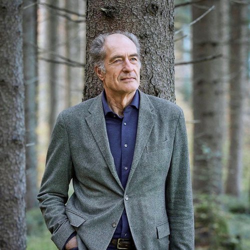 Wissen, das inspiriert: Unsere Vortragsreihe greift Themen auf, die das Leben bereichern. Älterer Mann lehnt im Wald an einem Baum mit Hände in den Taschen