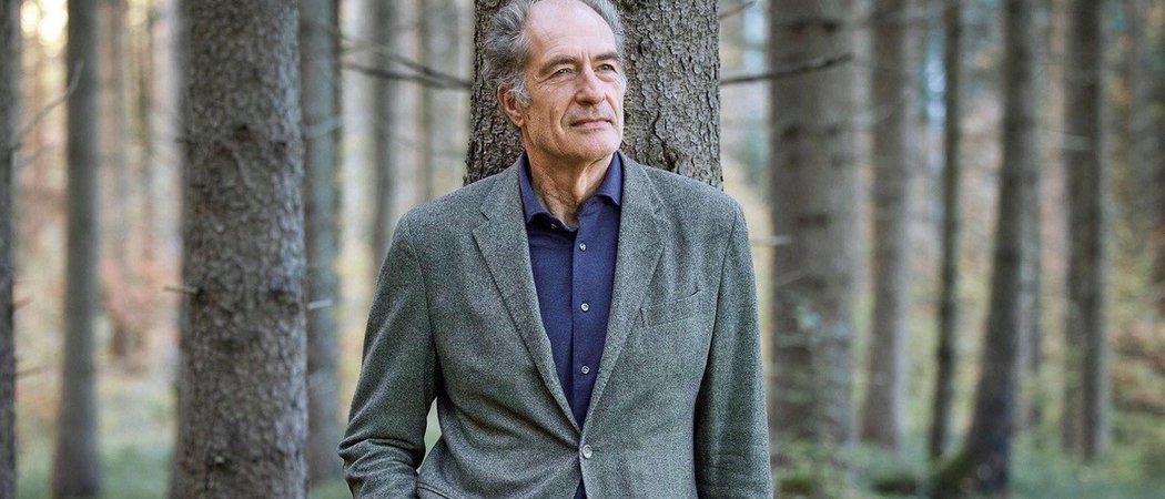 Wissen, das inspiriert: Unsere Vortragsreihe greift Themen auf, die das Leben bereichern. Älterer Mann lehnt im Wald an einem Baum mit Hände in den Taschen