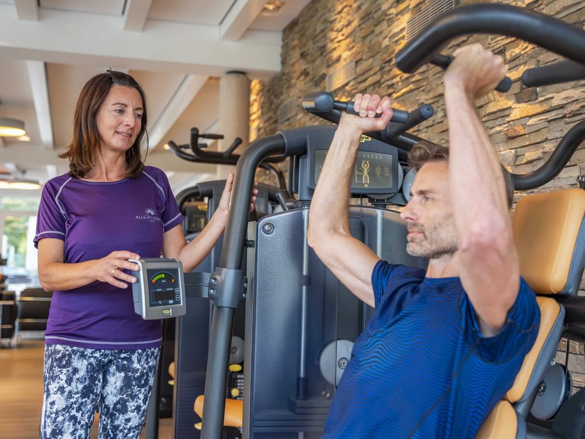 Ihr Hotel mit Fitnessstudio in Bayern Frau betreut Mann beim Training an Fitnessgerät im Fitnessstudio