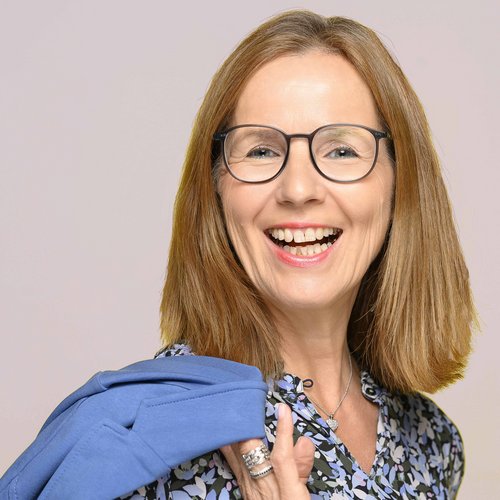 Wissen, das inspiriert: Unsere Vortragsreihe greift Themen auf, die das Leben bereichern. Lächelnde Frau mit Brille, Blumenbluse und blauem Pullover über der Schulter