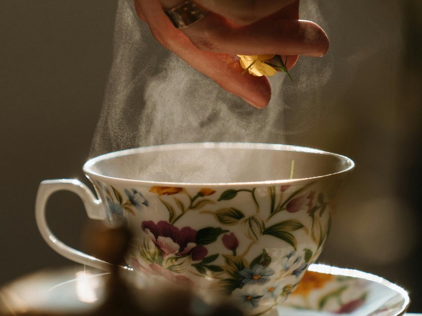 Allgäu Sonne – Ihr Ayurveda-Hotel im Allgäu Hand gibt Blume in dampfende Teetasse mit floralem Muster