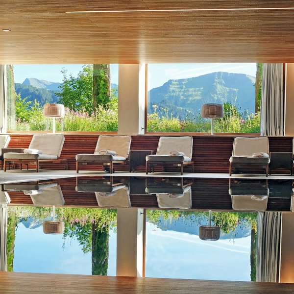 Ihr Wellnesshotel im Allgäu Innenpool mit Liegestühlen und Bergblick durch große Fenster