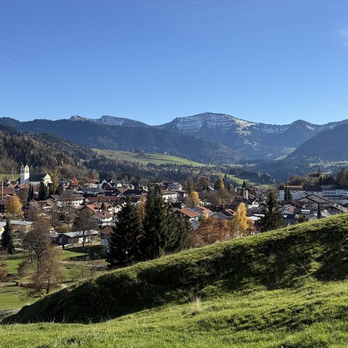 Die Tipps aus dem Wanderhotel im Allgäu Blick auf ein Dorf mit Kirche und schneebedeckten Bergen unter klarem Himmel
