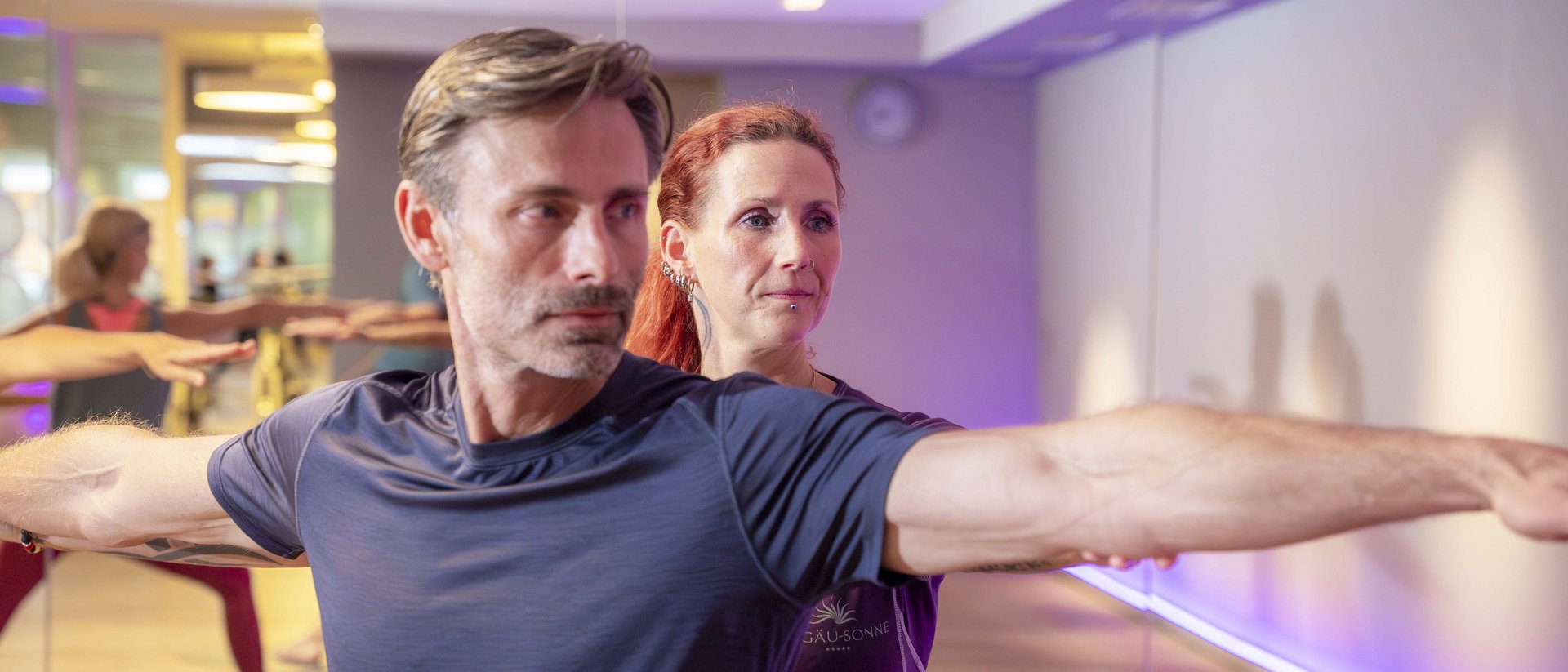 Your sports hotel in Allgäu: Allgäu Sonne Yoga instructor assists man with stretching exercise in bright gym