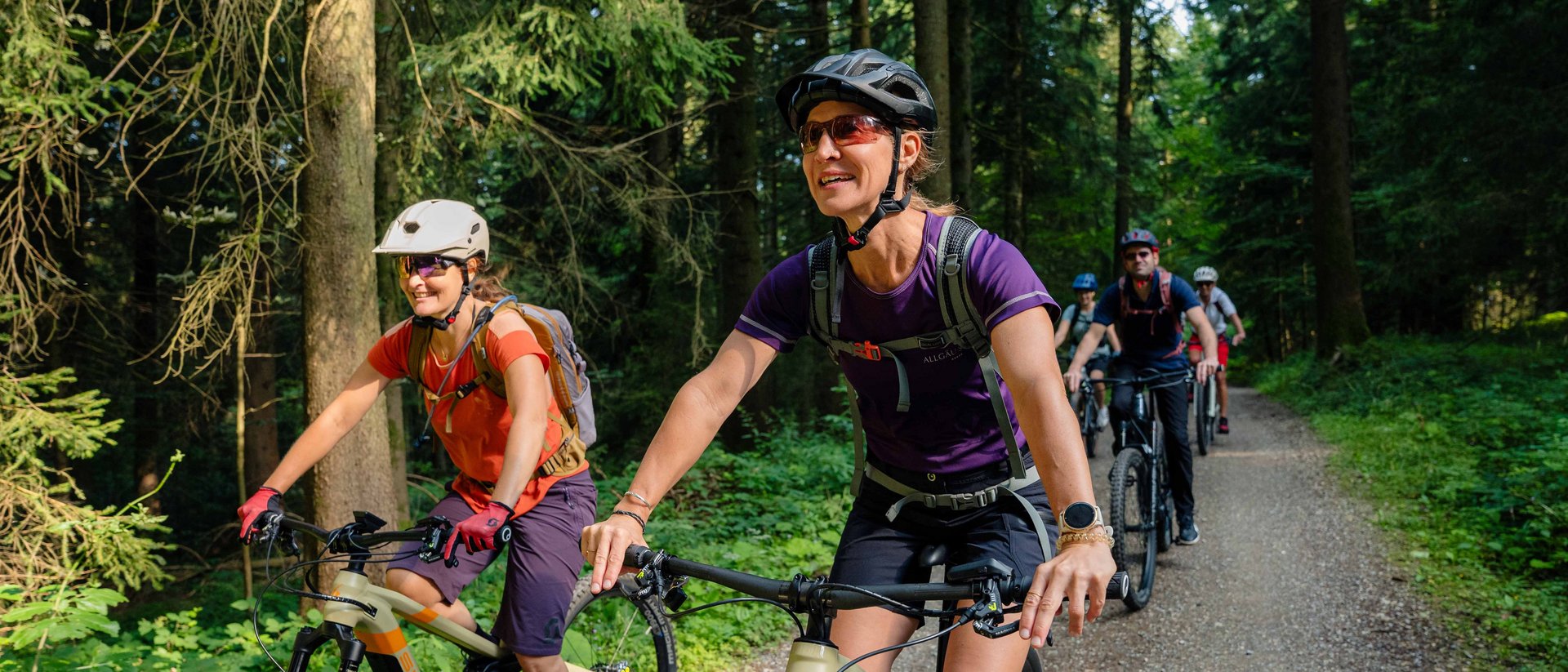 Sportwochen in unserem Fitnesshotel Gruppe von Menschen beim Mountainbiken auf einem Waldweg an einem sonnigen Tag