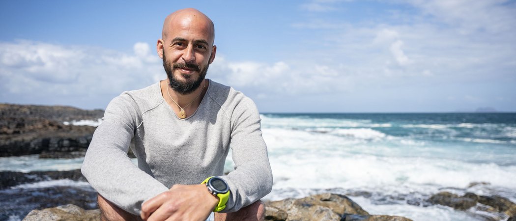 Wissen, das inspiriert: Unsere Vortragsreihe greift Themen auf, die das Leben bereichern. Mann mit Bart und grauem Pullover sitzt auf Felsen am Meer bei sonnigem Wetter