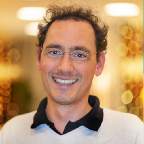 Wissen, das inspiriert: Unsere Vortragsreihe greift Themen auf, die das Leben bereichern. Lächelnder Mann mit Brille und lockigem Haar vor beleuchtetem Hintergrund