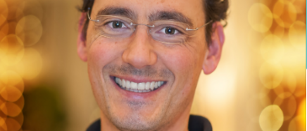 Wissen, das inspiriert: Unsere Vortragsreihe greift Themen auf, die das Leben bereichern. Lächelnder Mann mit Brille und lockigem Haar vor beleuchtetem Hintergrund