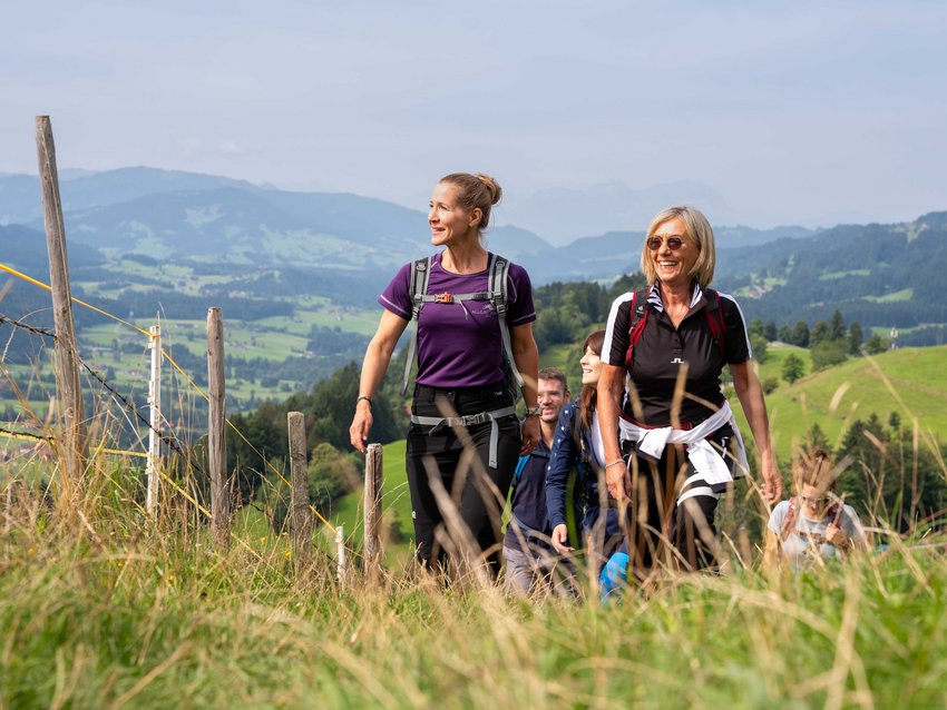 Your sports hotel in Allgäu: Allgäu Sonne Group of people hiking on a grassy trail in a mountainous landscape