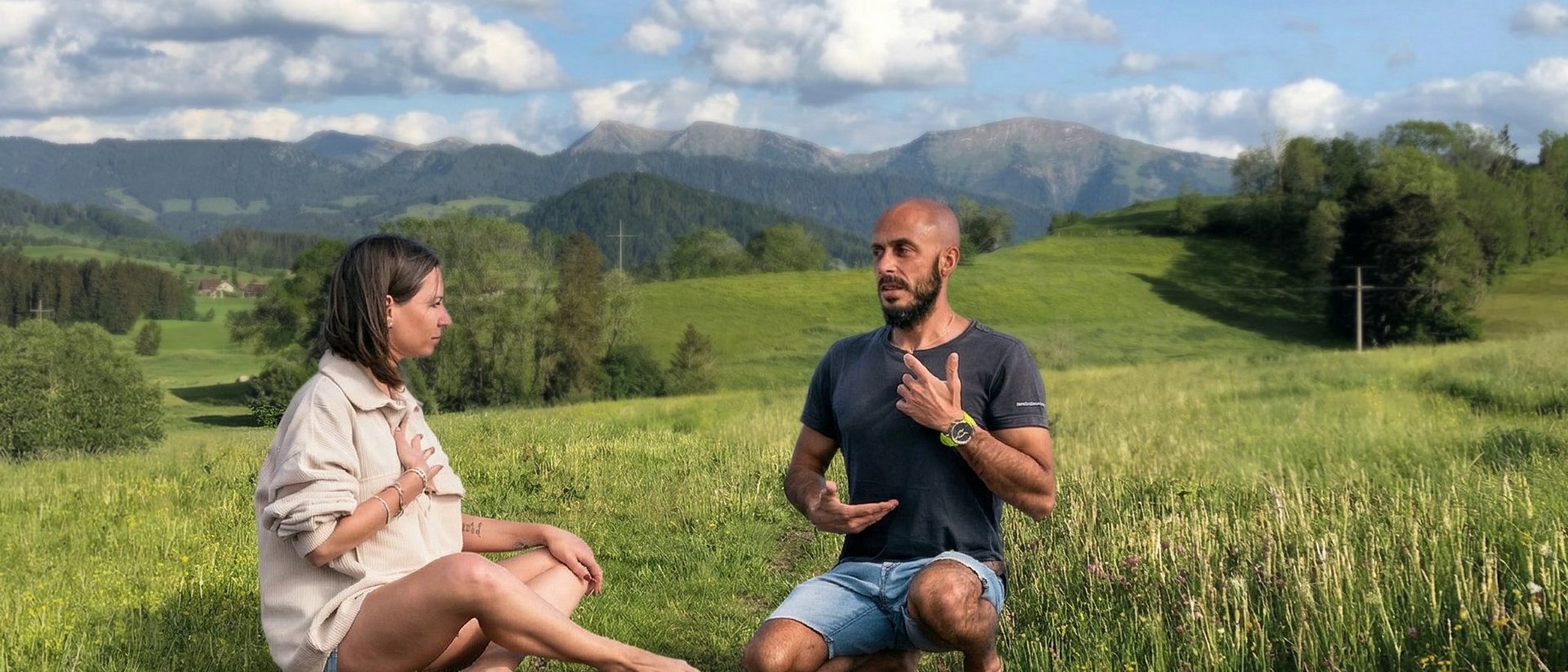 Das Breathwork Retreat Zwei Menschen meditieren barfuß auf einer Wiese mit Bergkulisse im Hintergrund