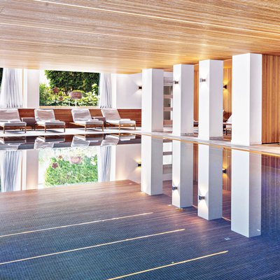 Wellness im Allgäu: 5-Sterne-Kosmetik Innenansicht eines modernen Hallenbads mit Liegestühlen und großen Fenstern