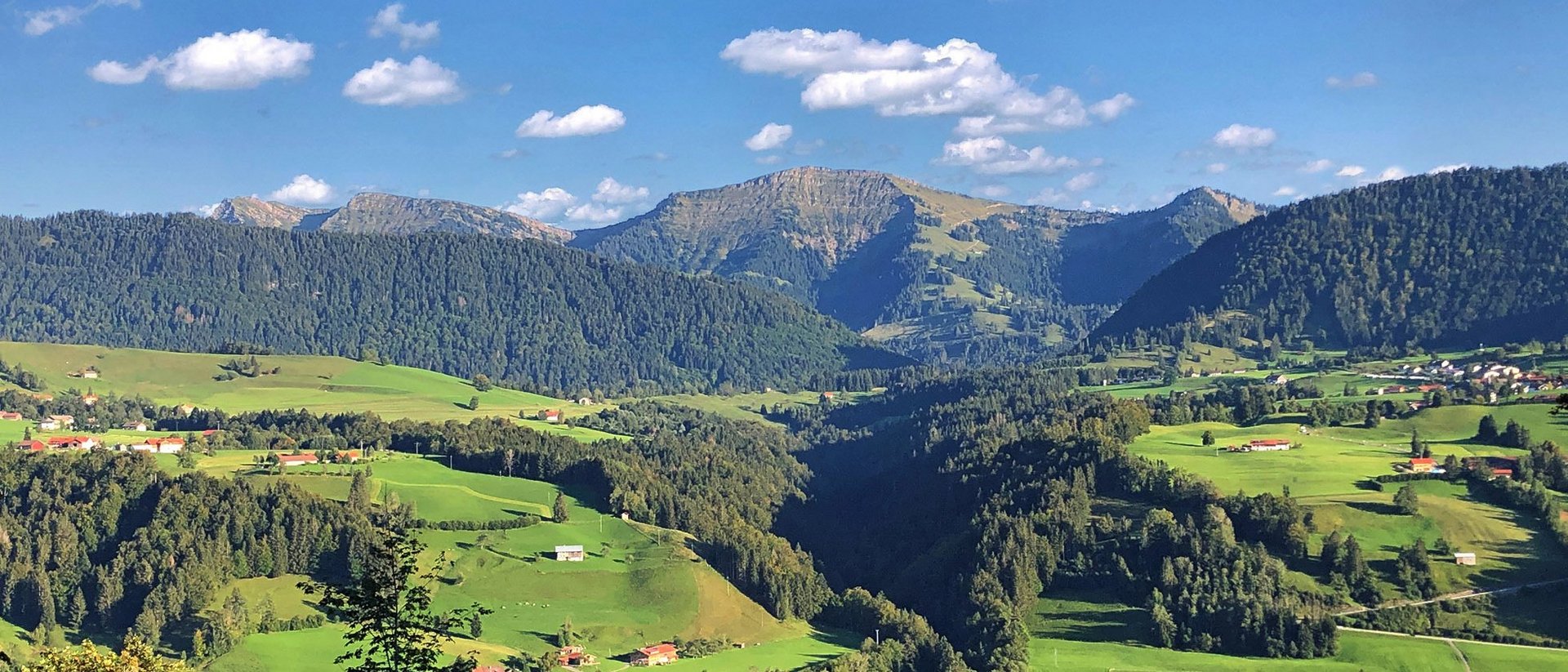 Wissen, das inspiriert: Unsere Vortragsreihe greift Themen auf, die das Leben bereichern. Grüne Hügel und Berge unter blauem Himmel mit vereinzelten Wolken