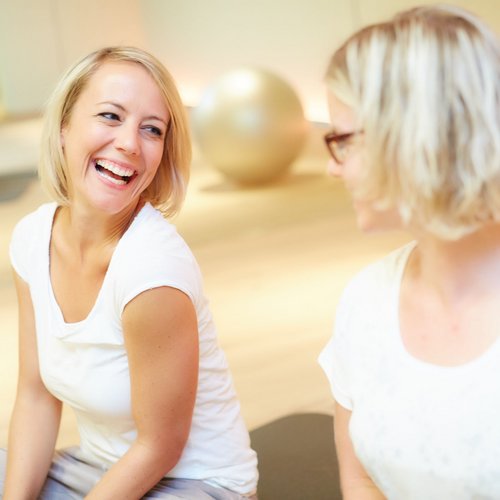 Das Breathwork Retreat Zwei Frauen sitzen sich lächelnd in einem hellen Raum mit Gymnastikbällen gegenüber