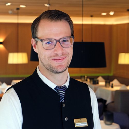 Our mission: your dream holiday in Oberstaufen Smiling male restaurant manager wearing glasses and name tag in dining area