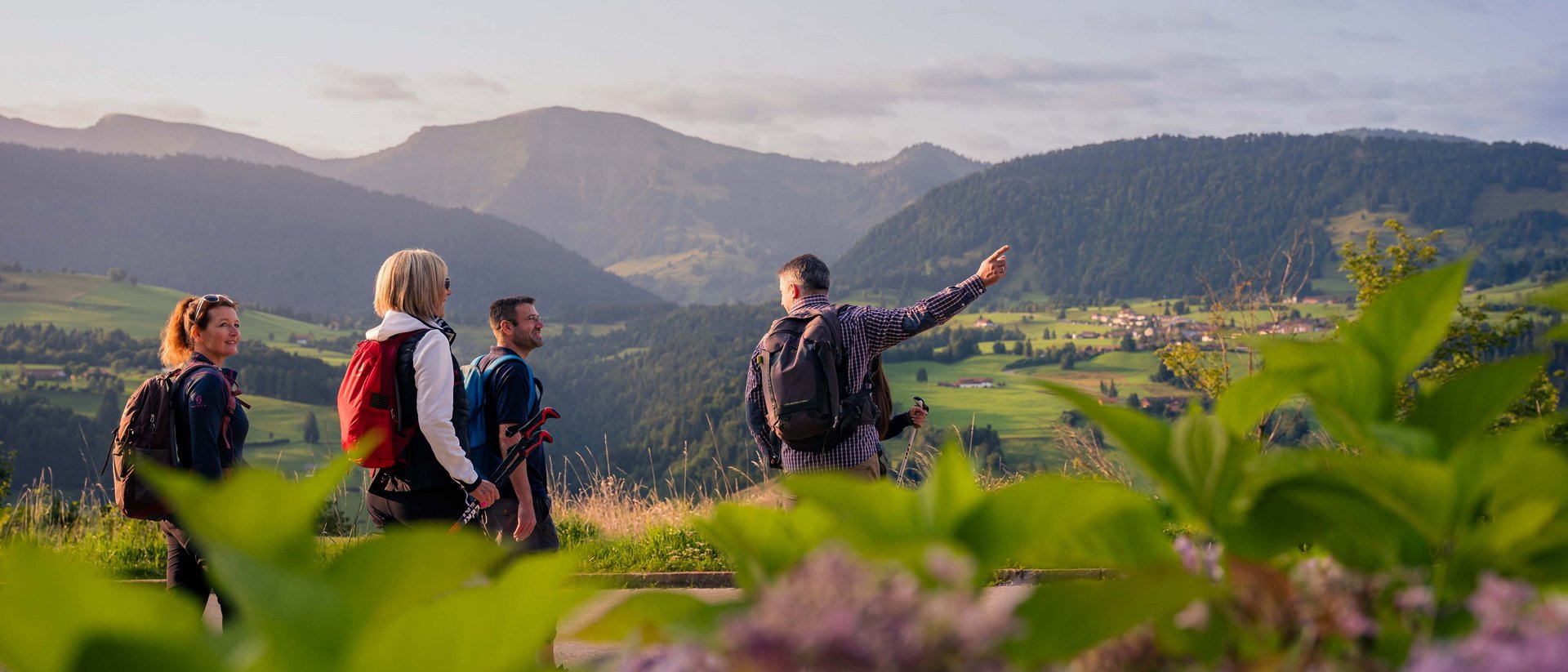 Your sports hotel in Allgäu: Allgäu Sonne Four hikers with backpacks looking at green mountains and valley at sunset