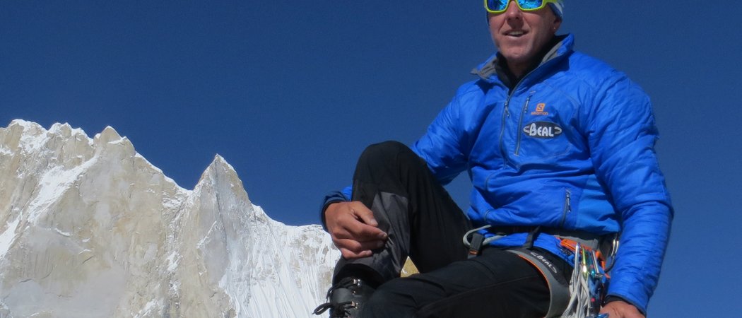 Wissen, das inspiriert: Unsere Vortragsreihe greift Themen auf, die das Leben bereichern. Bergsteiger in blauer Jacke auf Felsen mit schneebedecktem Berg und klarem Himmel
