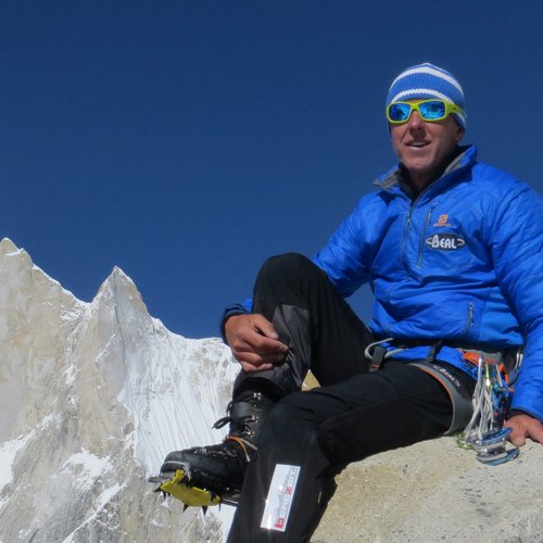 Wissen, das inspiriert: Unsere Vortragsreihe greift Themen auf, die das Leben bereichern. Bergsteiger in blauer Jacke auf Felsen mit schneebedecktem Berg und klarem Himmel