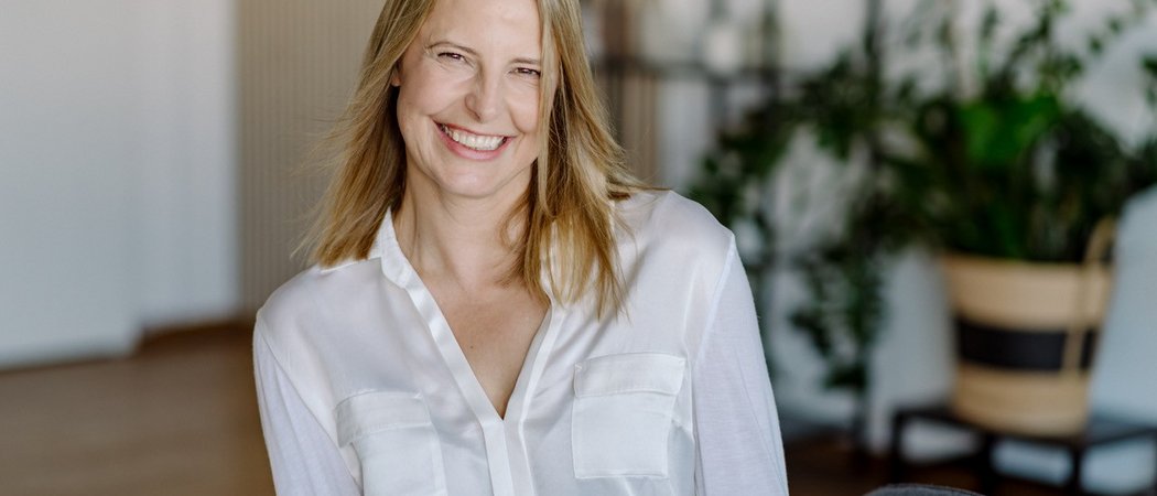 Wissen, das inspiriert: Unsere Vortragsreihe greift Themen auf, die das Leben bereichern. Lächelnde Frau mit weißer Bluse vor unscharfem Hintergrund im Innenraum