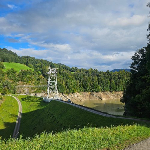 Ihr E-Bike-Hotel in Deutschland: Allgäu Sonne Stausee mit Damm und Stromleitung in einer grünen Hügellandschaft