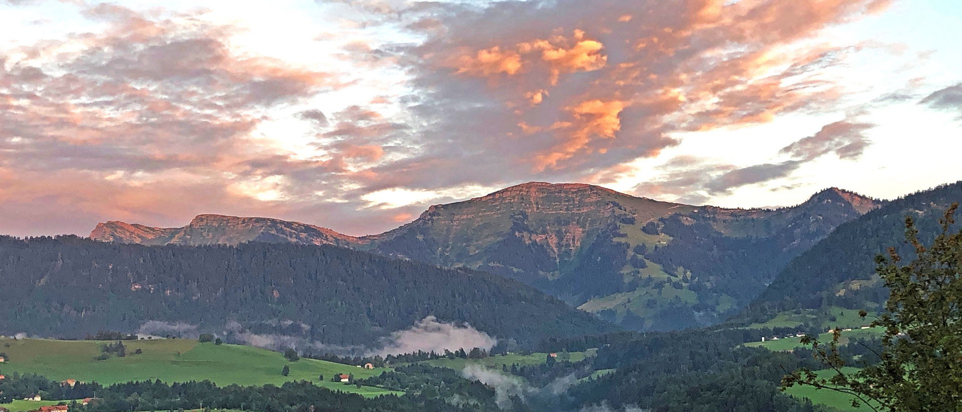 Wissenswertes übers Allgäu Berglandschaft mit grünen Wiesen und wolkigem Sonnenuntergangshimmel