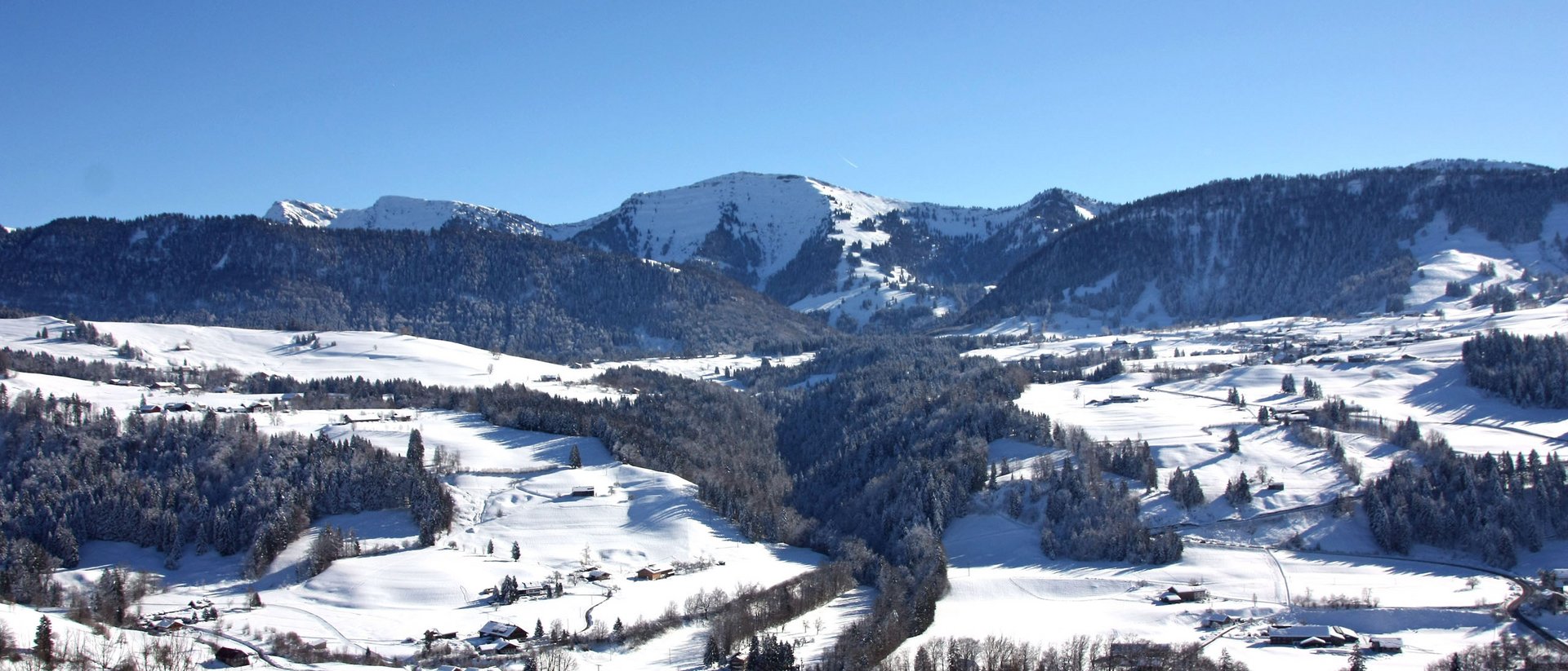 Wissenswertes übers Allgäu Winterlandschaft mit schneebedeckten Bergen und Häusern unter klarem blauem Himmel