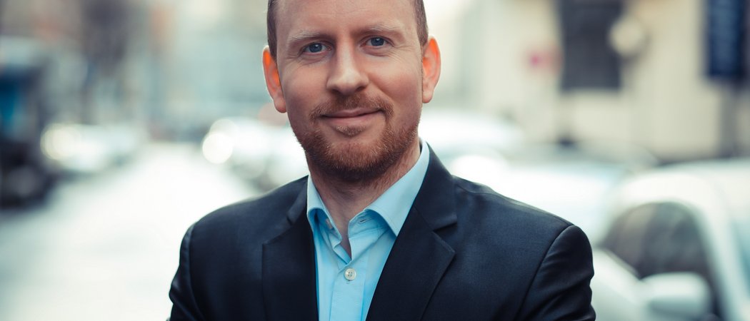 Wissen, das inspiriert: Unsere Vortragsreihe greift Themen auf, die das Leben bereichern. Porträt eines lächelnden Mannes in Anzug auf belebter Straße