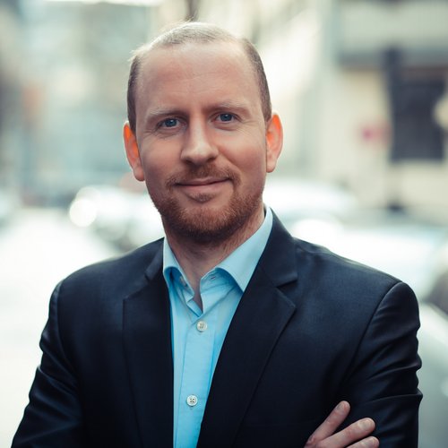 Wissen, das inspiriert: Unsere Vortragsreihe greift Themen auf, die das Leben bereichern. Porträt eines lächelnden Mannes in Anzug auf belebter Straße