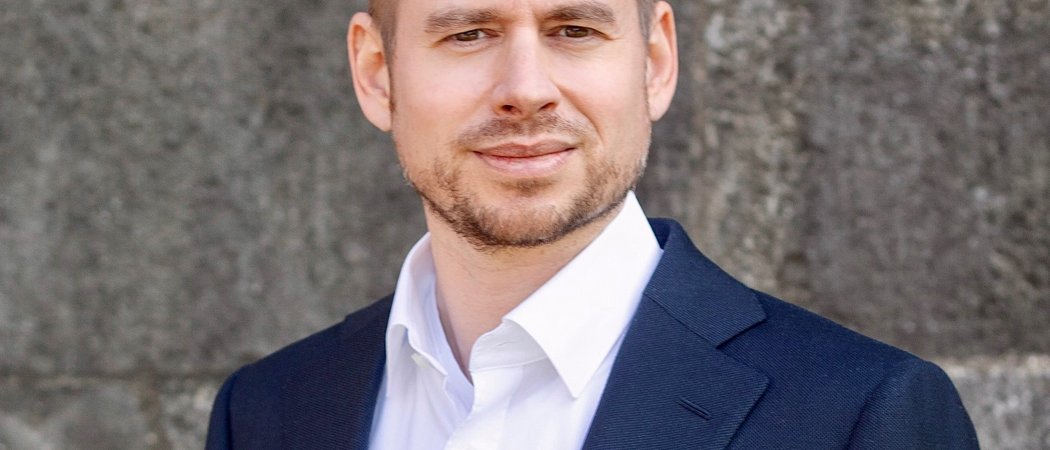 Wissen, das inspiriert: Unsere Vortragsreihe greift Themen auf, die das Leben bereichern. Porträt eines Mannes in blauem Anzug und weißem Hemd vor grauer Wand