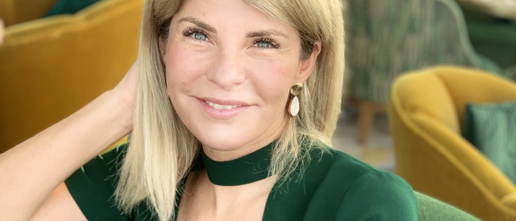 Wissen, das inspiriert: Unsere Vortragsreihe greift Themen auf, die das Leben bereichern. Frau mit blondem Haar und grünem Kleid sitzt und lächelt in einem Café