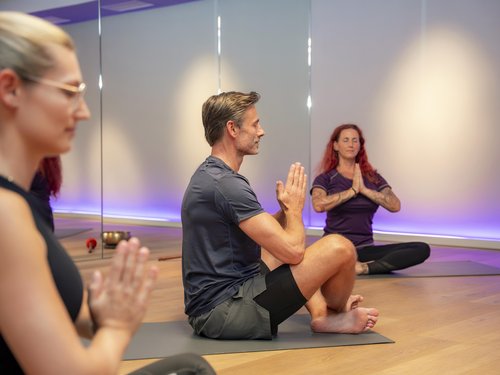 Sportwochen in unserem Fitnesshotel Menschen sitzen im Schneidersitz und meditieren in einem Yoga-Studio mit gedämpftem Licht.