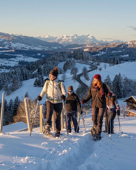 Ihr Wellnesshotel im Allgäu Gruppe beim Schneeschuhwandern in verschneiter Berglandschaft bei Sonnenuntergang