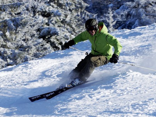 Sportwochen in unserem Fitnesshotel Mann in grüner Jacke beim Skifahren auf verschneiter Piste